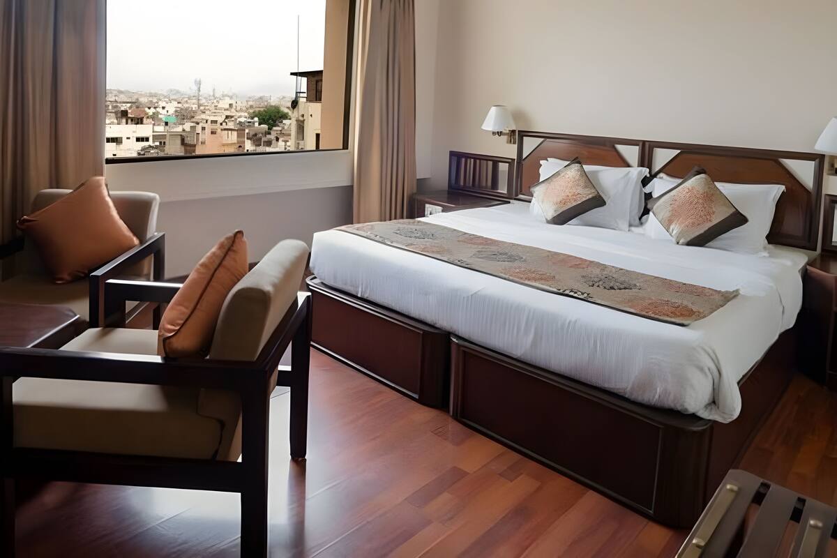 Ein Hotelzimmer mit einem großen Bett, einem Schreibtisch, einem Sessel und Blick auf die Stadt.