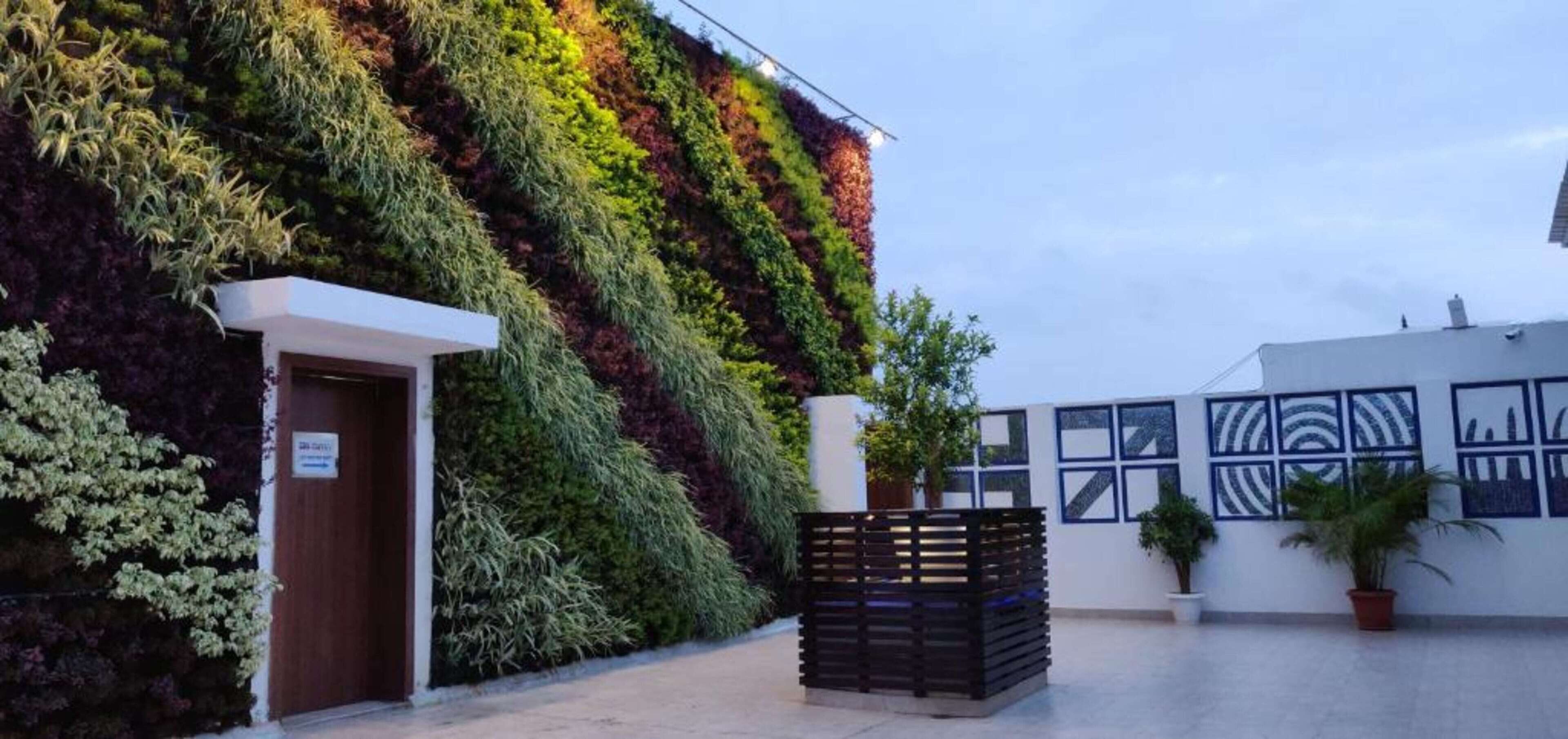 Un edificio con fachada ajardinada vertical, entrada blanca y ventanas con diseños.