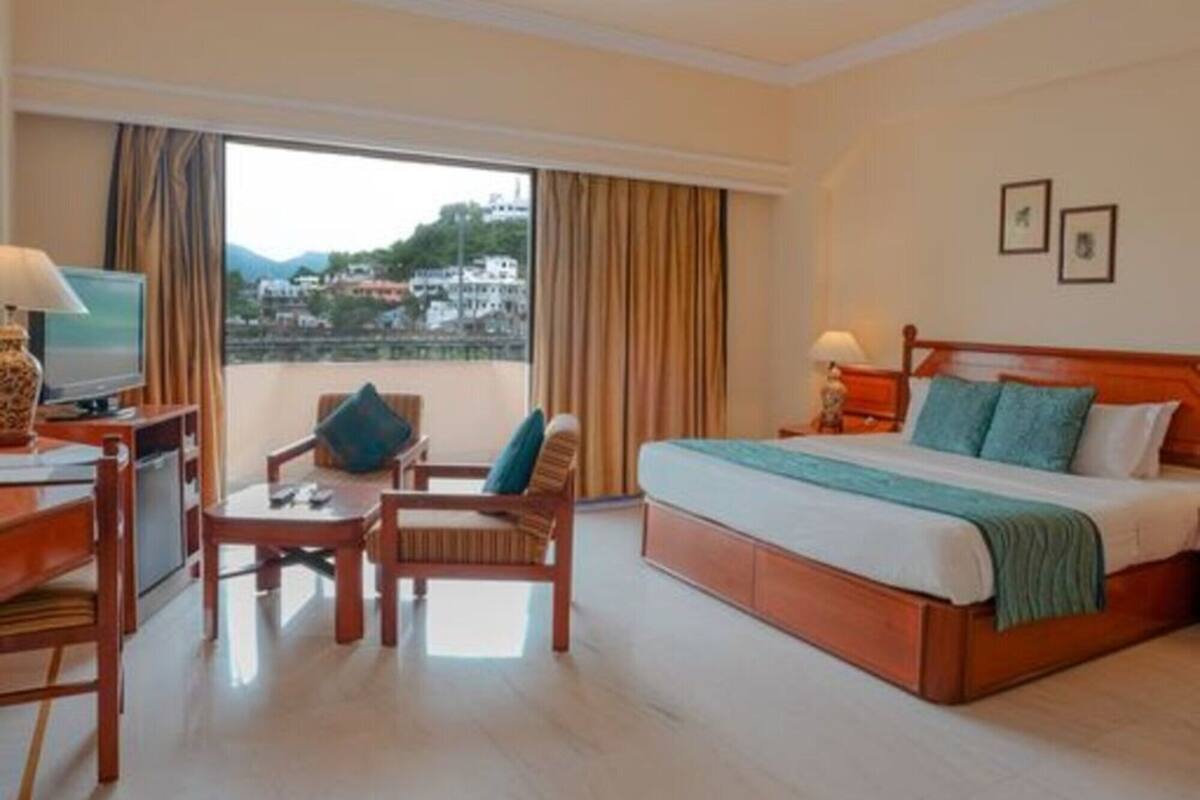 Ein Hotelzimmer mit Bett, Schreibtisch mit Stuhl, Fernseher und Blick auf eine Stadtlandschaft durch das Fenster.