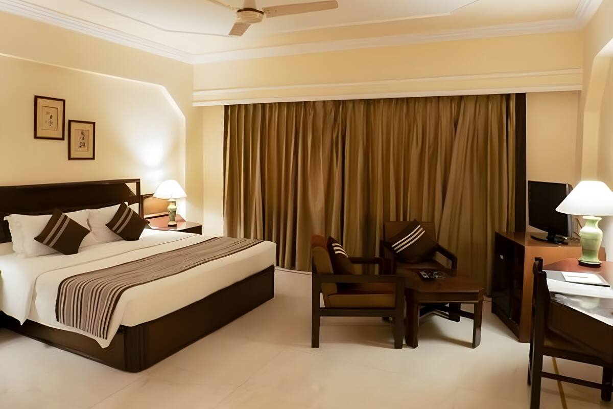 Ein Hotelzimmer mit Bett, Schreibtisch, Stuhl, Fernseher und Deckenventilator.