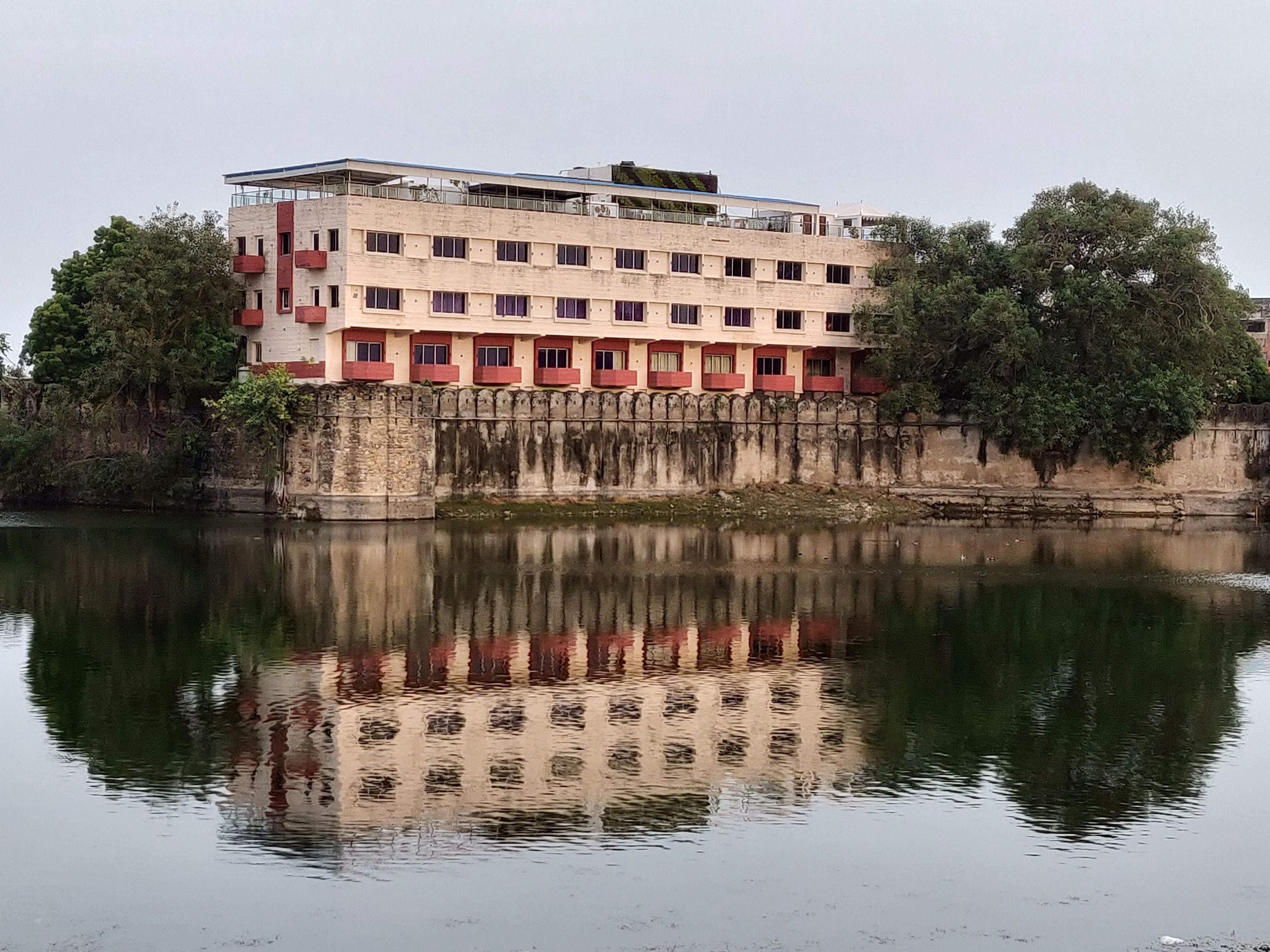 A multi-story building with a reflection in the water, featuring balconies and a flat roof.