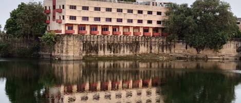 A multi-story building with a reflection in the water, featuring balconies and a flat roof.