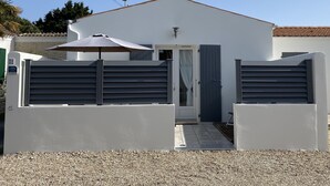 Une maison moderne avec une façade blanche, une porte grise et un portail gris.