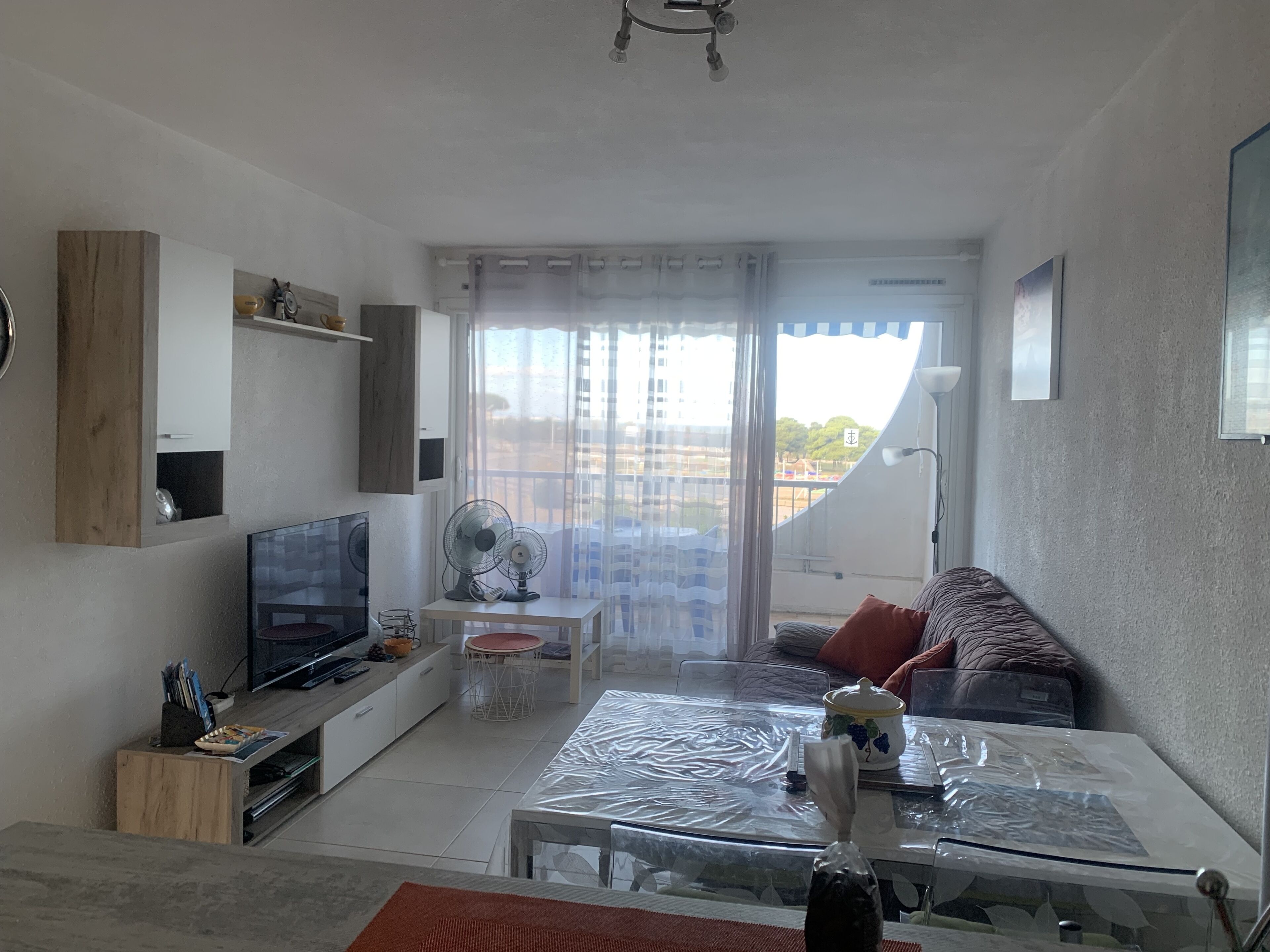 Un saló modern amb un televisor de pantalla plana, dos ventiladors de peu, una taula de cafè de vidre i un sofà amb coixins.