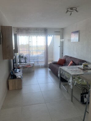 A modern living room with a sofa, a dining table, and a TV mounted on the wall.