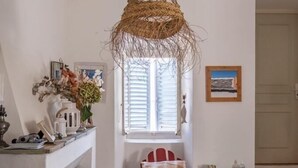 A cozy dining area with a woven pendant light, a fireplace, a dining table with a vase of flowers, and a window with shutters. - The village candy (Meria)