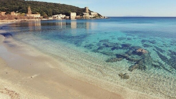 A clear coastal beach with a sandy shore and a small village with buildings and a tower. - The village candy (Meria)