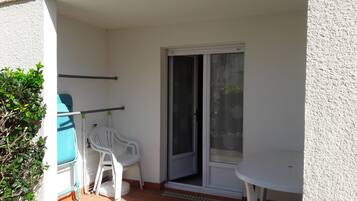 Un balcón con una silla blanca, una mesita y una puerta corrediza de vidrio.