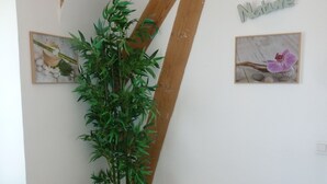Een kamer met een schuin houten plafond, een bamboe plant, een klein Boeddhabeeld, een rond houten krukje en twee ingelijste foto’s aan de wanden.