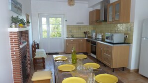 Een moderne keuken met houten kastjes, een metselwerk openhaard, en een eethoek voor zes personen, compleet met gele borden en glazen.