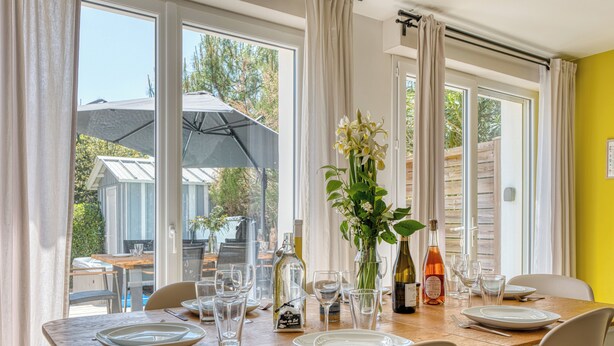 A dining area with a table set for four, a vase with flowers, and a bottle of wine.