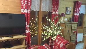 Ett mysigt vardagsrum med en soffa i trä, en tv och en julgran med ljus.