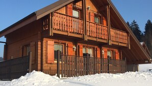 En stuga av trä med en balkong, omgiven av snö.