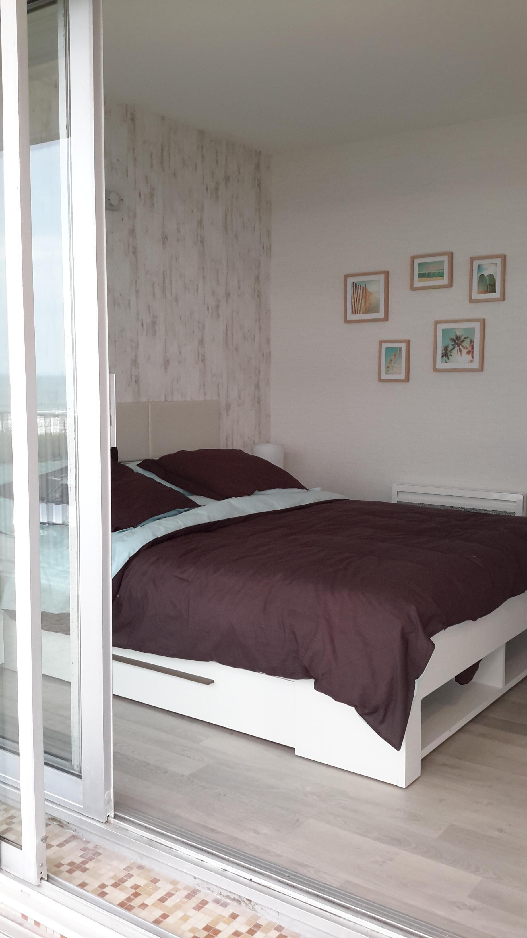 Un dormitorio con una cama, una ventana y una pared decorada con marcos.