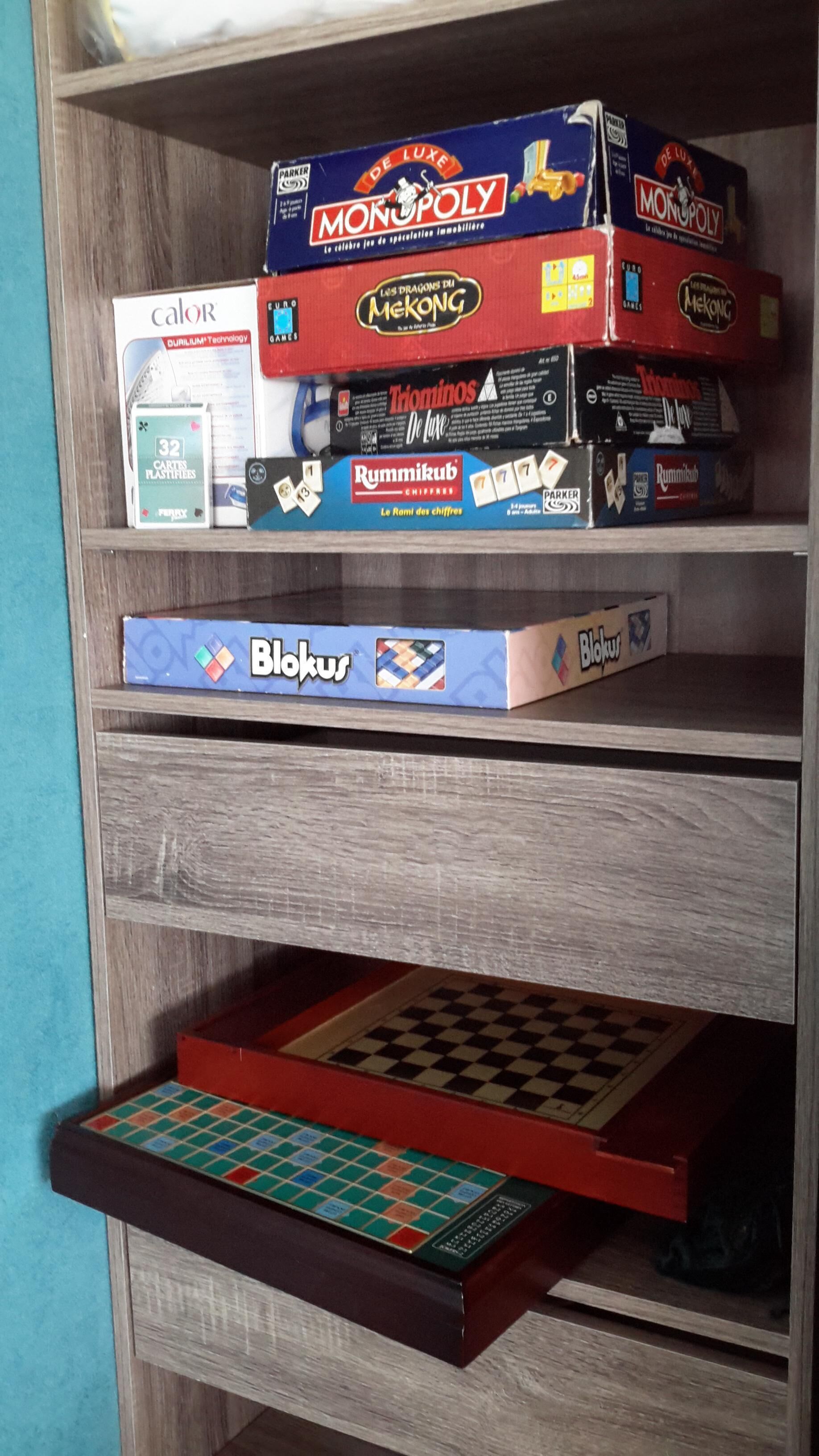 Une étagère en bois sur laquelle sont rangés divers jeux de société, notamment Monopoly et Blokus.