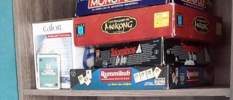 Une étagère en bois sur laquelle sont rangés divers jeux de société, notamment Monopoly et Blokus.