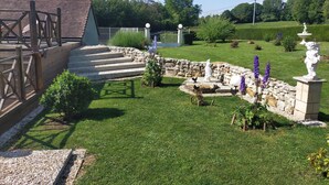 Een tuin met stenen traptreden, een houten terras en diverse beelden.
