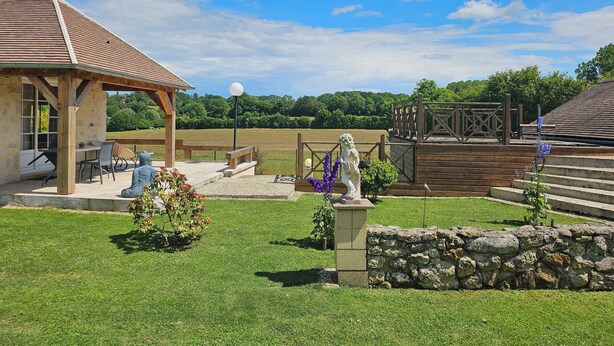 Een rustieke buitenruimte met een stenen tafel en stoelen, een houten pergola en een standbeeld.