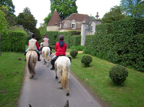 A pathway with people riding horses, surrounded by greenery and a historic building in the background. - Gite in the heart of the Perche, with garden, 2 terraces and 2 beds, Le Pierra (Perche En Nocé)