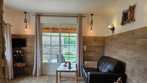 Een gezellige kamer met een houten vloer, een zwarte leren bank, een klein tafeltje met een lamp en een televisie op een standaard.