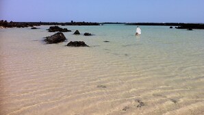 Uma praia com águas cristalinas, rochas e uma pessoa ao longe.