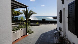 Um corredor estreito ao ar livre com vista para o mar, um edifício branco com persianas pretas e um banco.