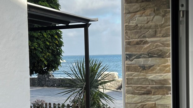 Visão através de uma porta para uma parede de pedra e um pátio com vista para o oceano.