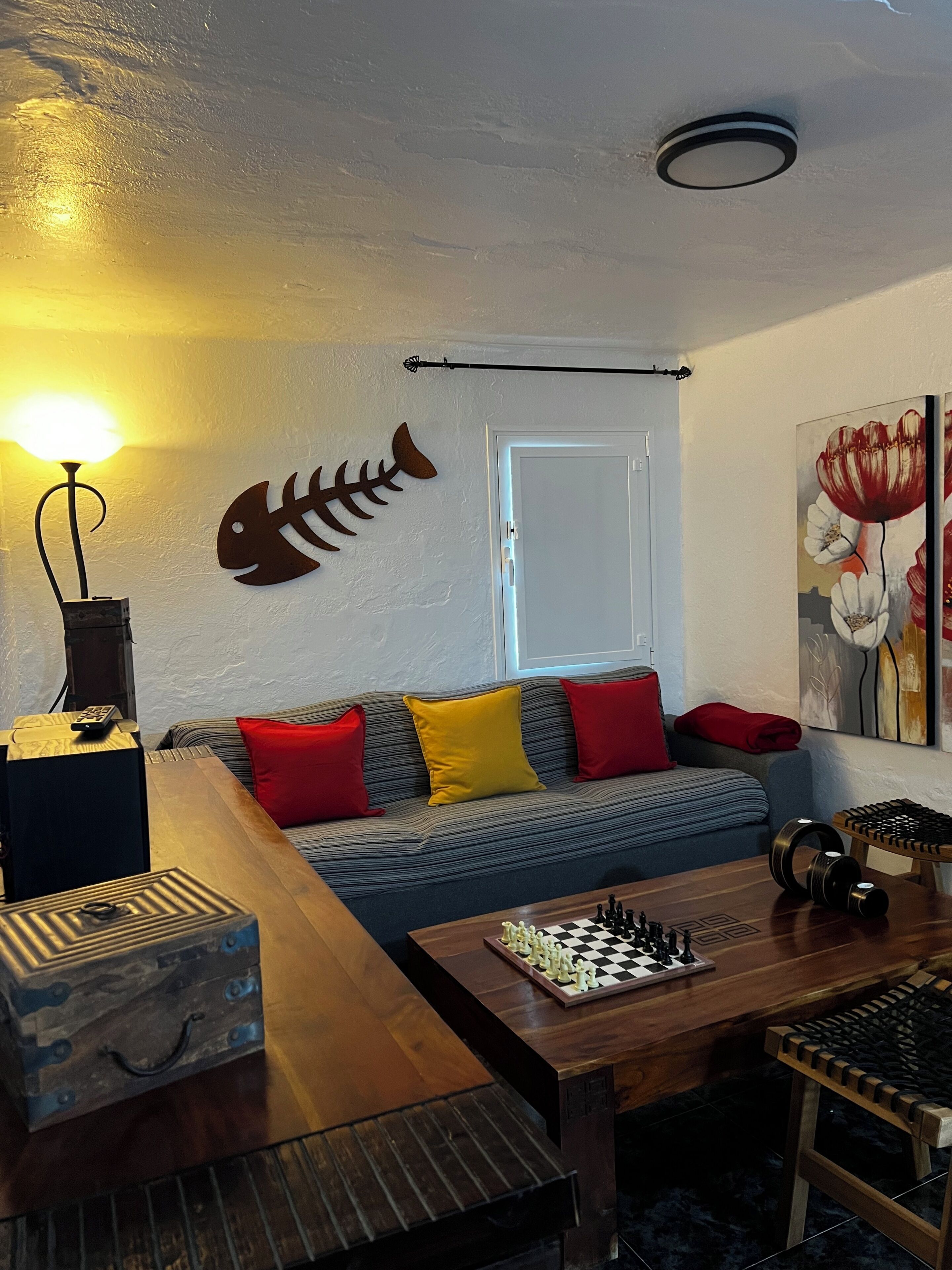 A living room with a sofa, a chess table, a lamp, and a fish wall decoration.