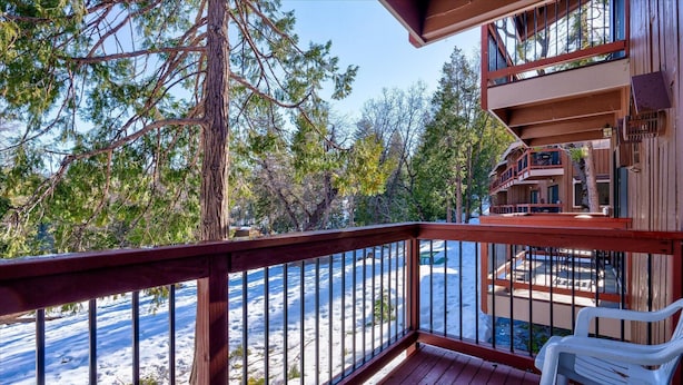 A wooden deck with a railing overlooking a snowy landscape and trees.