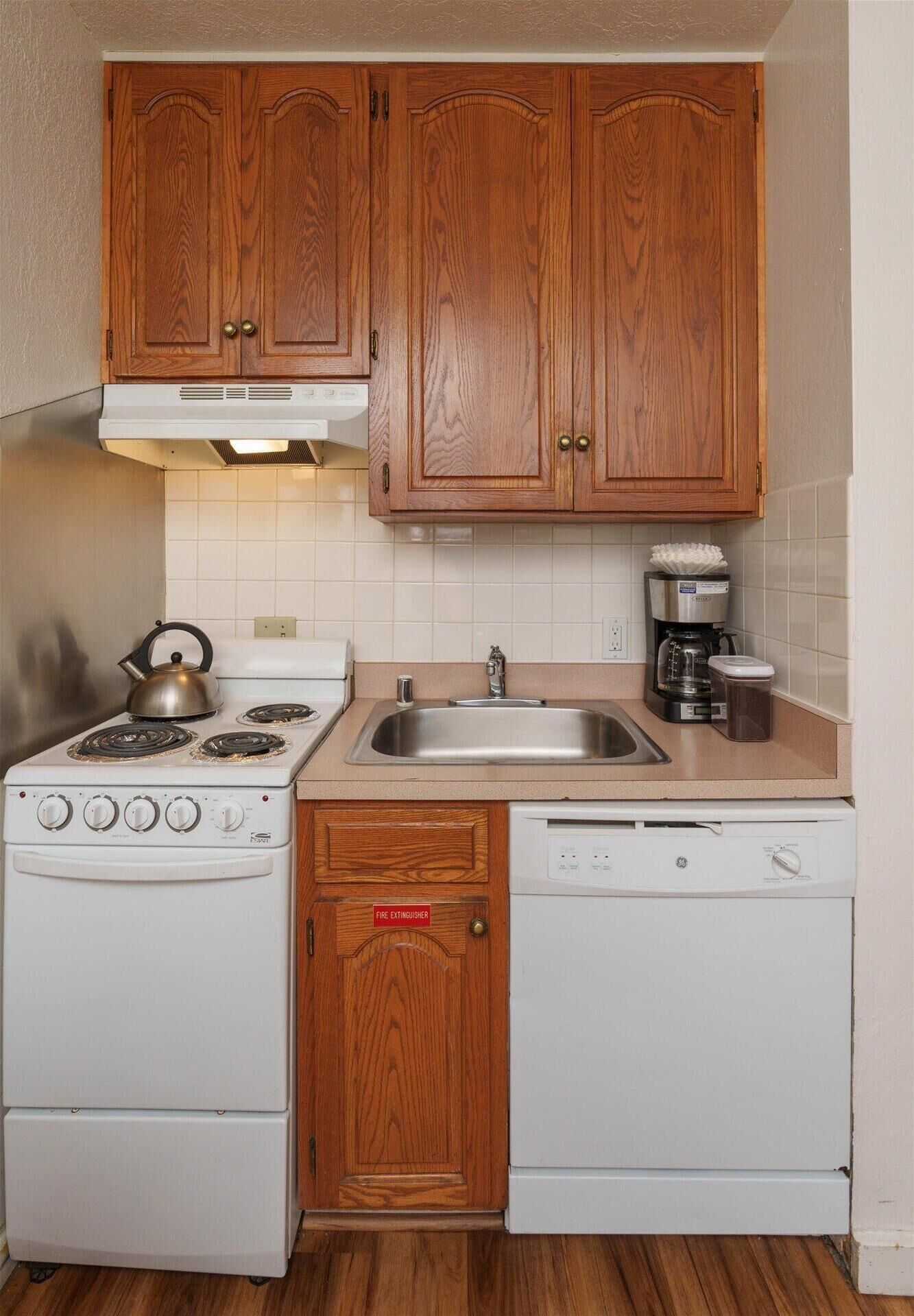 A compact kitchen with wooden cabinets, a white stove, a sink, and a dishwasher.