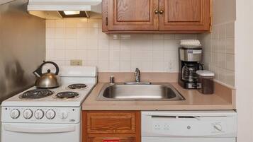 A compact kitchen with wooden cabinets, a white stove, a sink, and a dishwasher.