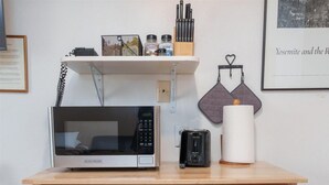 A wooden kitchen cart with a microwave, toaster, and various kitchen utensils.