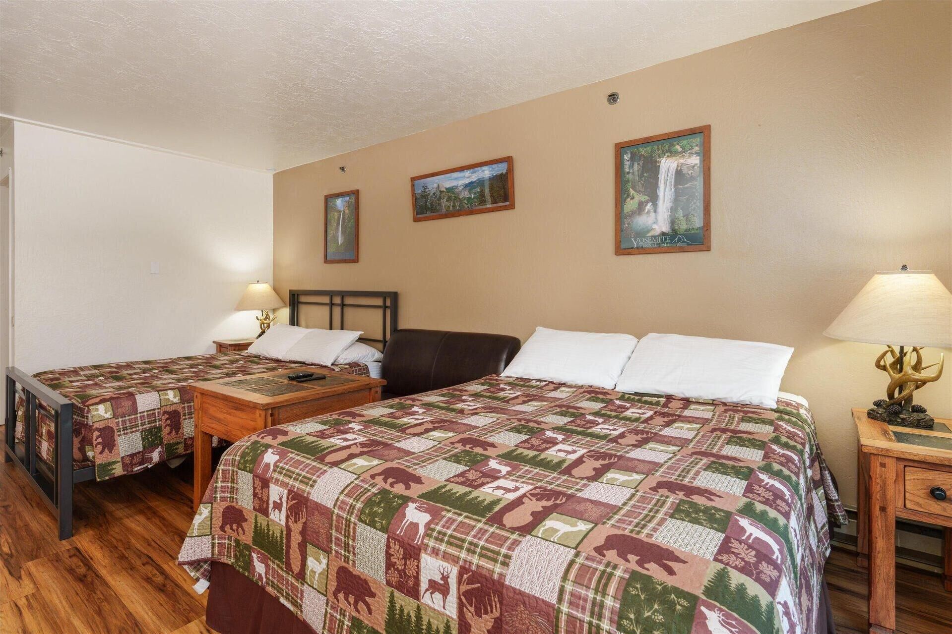 A room with two beds, each with a quilted blanket featuring animal prints, a wooden nightstand with a lamp, and a wall-mounted picture frame.