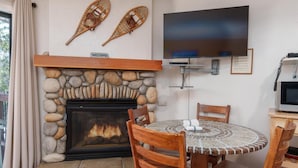 A cozy living room with a stone fireplace, a round table with chairs, a flat-screen TV, and two wooden sleds on the wall.