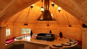 Una baita in legno con soffitto alto, un'isola centrale con un piano cottura e un tavolo da pranzo per quattro persone.