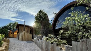 Una baita di legno con un vialetto sterrato che conduce a un recinto in legno e un'ampia finestra circolare.