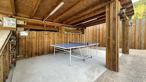 Un tavolo da ping pong in un'area delimitata da recinzioni in legno, con pavimento in cemento, travi in legno e parete in legno.