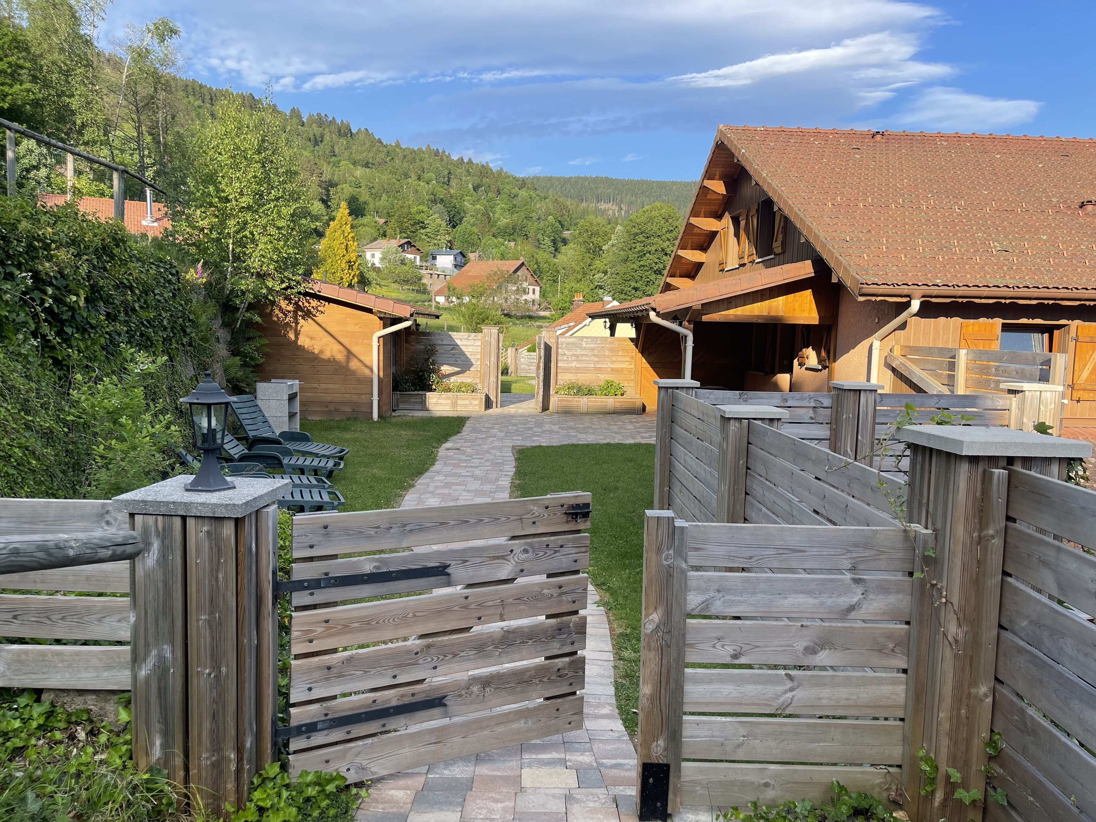 A wooden cabin with a tiled roof, surrounded by a wooden fence and a stone pathway.
