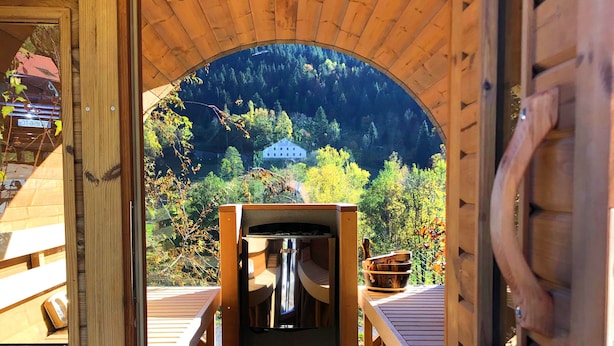 Una baita di legno con una veranda in legno che conduce a una zona salotto centrale con tavolo e sedie.