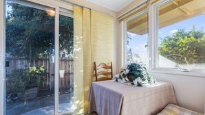 A room with a sliding glass door leading to a garden, a table with a tablecloth, and a window with a view of trees and a fence. - Beach House Perfect for your Next Getaway! (Morro Bay)