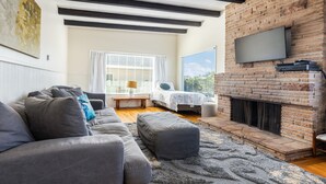 A modern living room with a grey sofa, a fireplace, and a television mounted on a brick wall. - Beach House Perfect for your Next Getaway! (Morro Bay)
