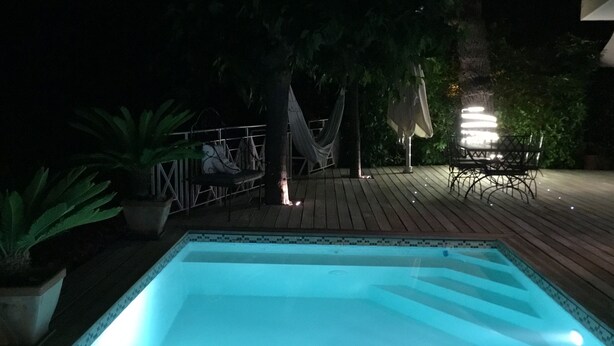 A swimming pool with a tiled edge, surrounded by a wooden deck and potted plants.