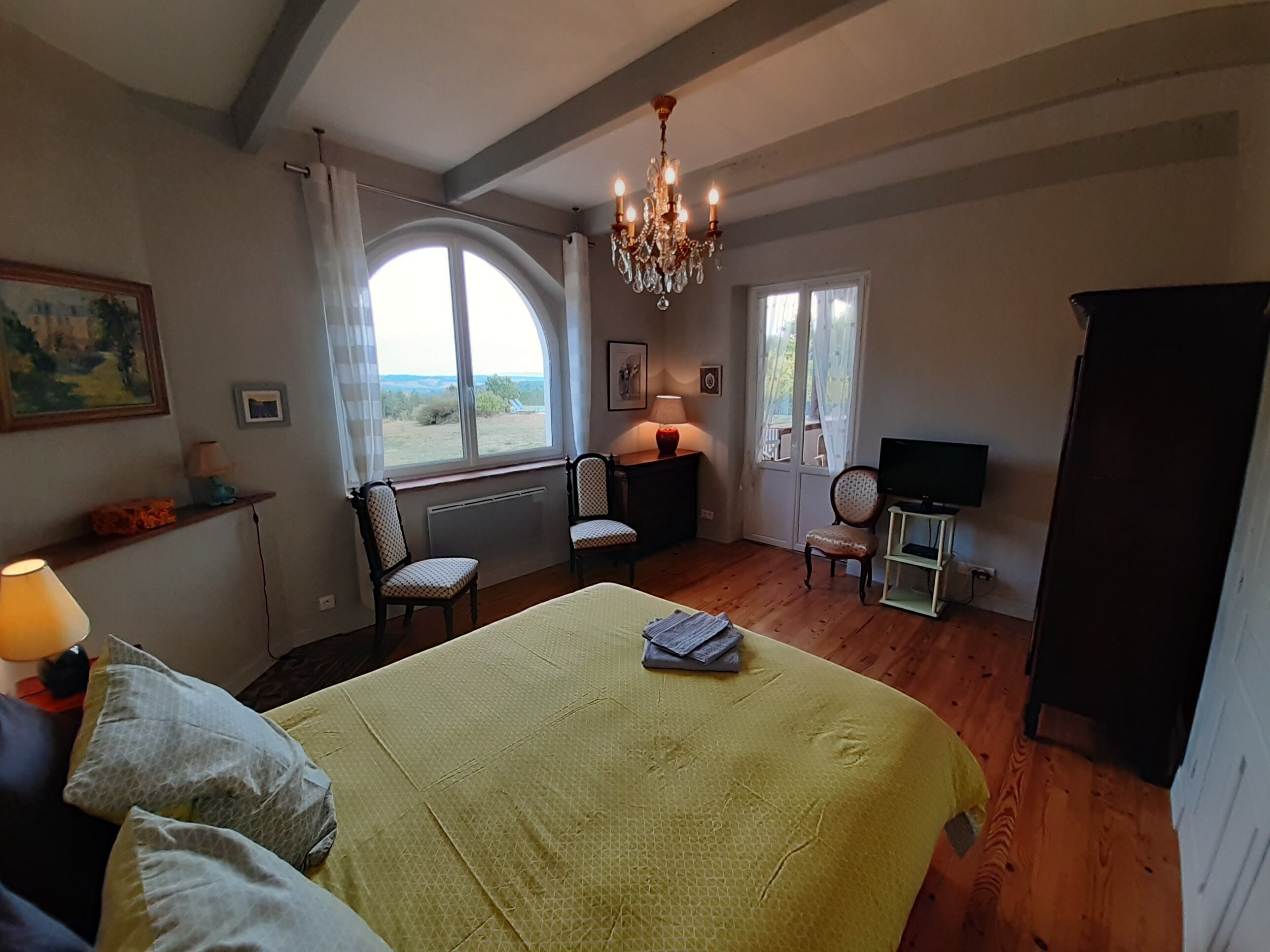 Une chambre à coucher avec un grand lit, deux fauteuils, un téléviseur et un lustre.