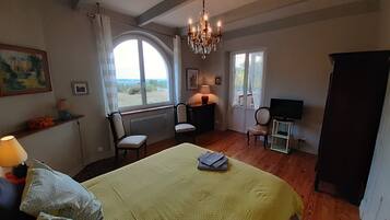Une chambre à coucher avec un grand lit, deux fauteuils, un téléviseur et un lustre.