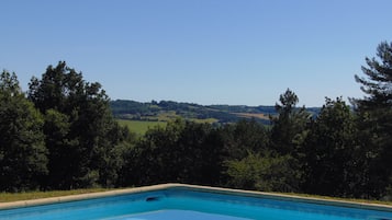 A swimming pool with a view of a hilly landscape and trees.