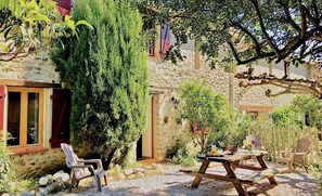 Un bâtiment en pierre doté d’un patio, d’un espace extérieur aménagé avec des sièges et d’un grand arbre.