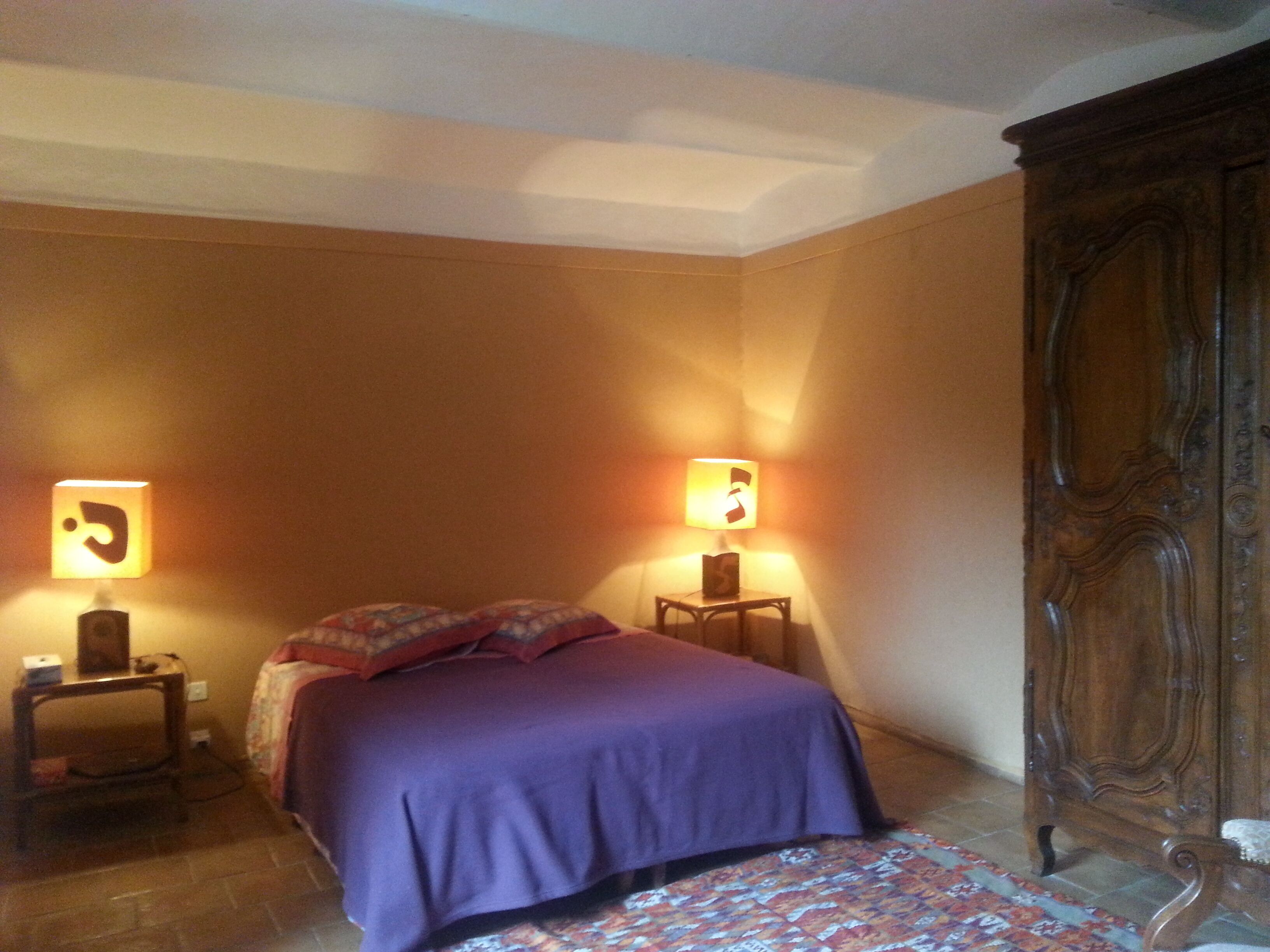 Une chambre à coucher avec un lit, deux lampes de chevet, une armoire en bois et un tapis à motifs.