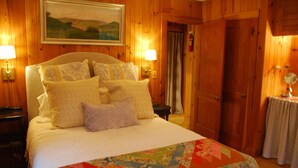 A wooden-paneled room with a bed, two wall-mounted lamps, and a painting above the bed. - Minutes To Town, Wooded 2 Acre Retreat (Highlands)