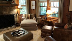 A cozy living room with a fireplace, leather sofas, a coffee table, and a television mounted on a stone wall. - Minutes To Town, Wooded 2 Acre Retreat (Highlands)