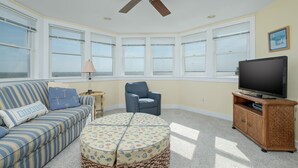 Una sala de estar con sofá, sillón, reposapiés, televisor y ventilador de techo.